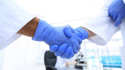 To hender med blå hansker hilser på hverandre på et sykehuslaboratorium