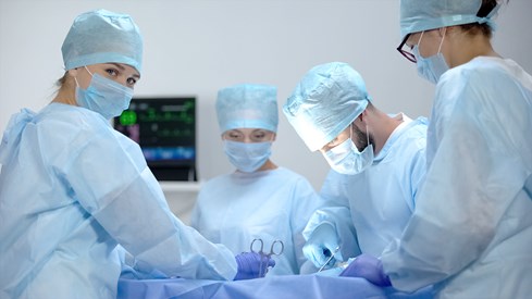 Fire kirurger i en operasjonssal, en av de ser inn i kamera