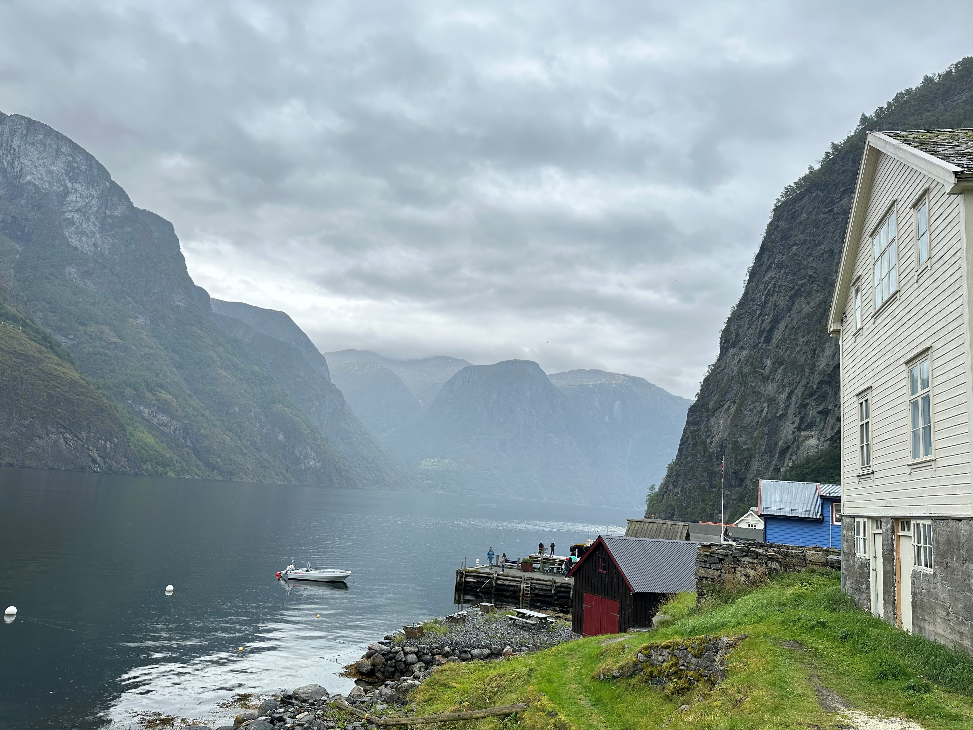 Aurlandsfjorden frå bryggja i Undredal i Aurland kommune. Bildet viser dei bratte fjellsidene som stuper ned i vatnet. Vêret er grått og overskya. EIn kan sjå husveggen på eit gammalt hus til høgre i bildet, og ein liten båt på fjorden.