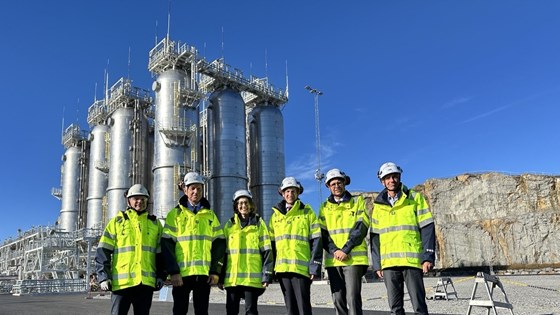 There is a picture of six people in protection gear in front of an industrial site. 