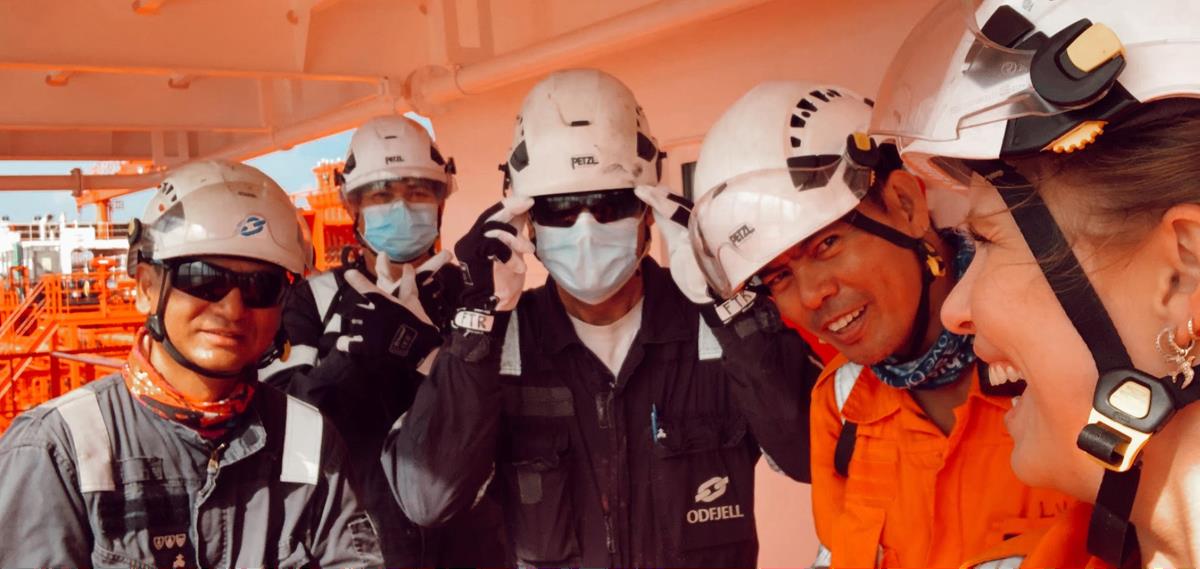 Fem sjøfolk kledd i arbeidsutstyr i godt humør.