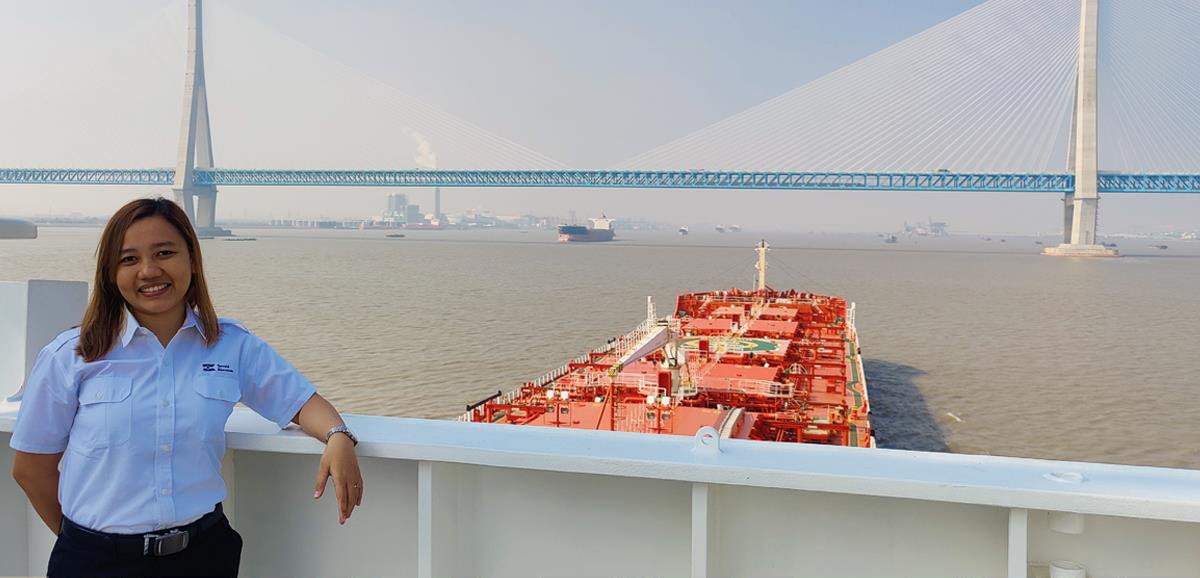 En kvinne om bord på et stort skip som seiler mot en bro som er synlig i bakgrunnen.