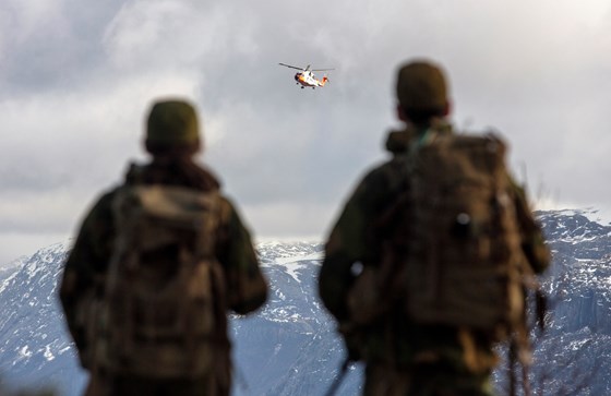 Bildet viser to soldater som ser på et Sar Queen-helikopter i luften