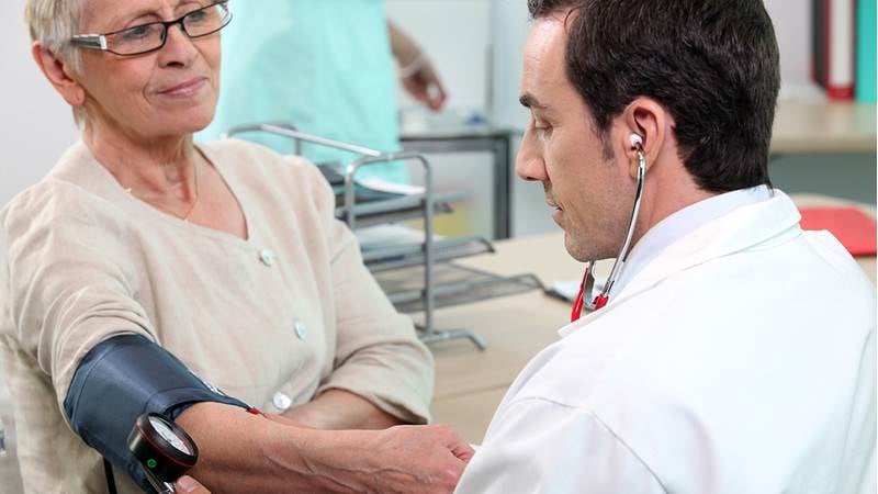 En mannlig lege måler blodtrykket til en eldre kvinnelig pasient