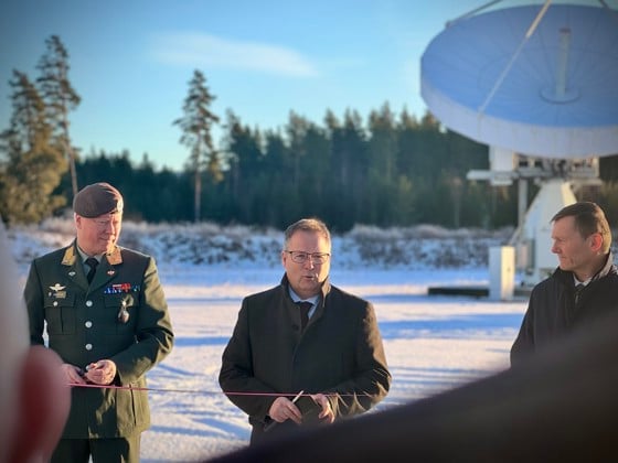 Forsvarsministeren og to andre står foran en stor antenne med snø og sol i bakgrunnen