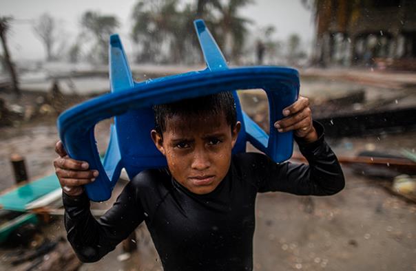 A child in Bilwi, Nicaragua, protects himself from the heavy rain with a plastic chair. He is standing in the spot where his house used to be, after it was destroyed by Hurricane Iota