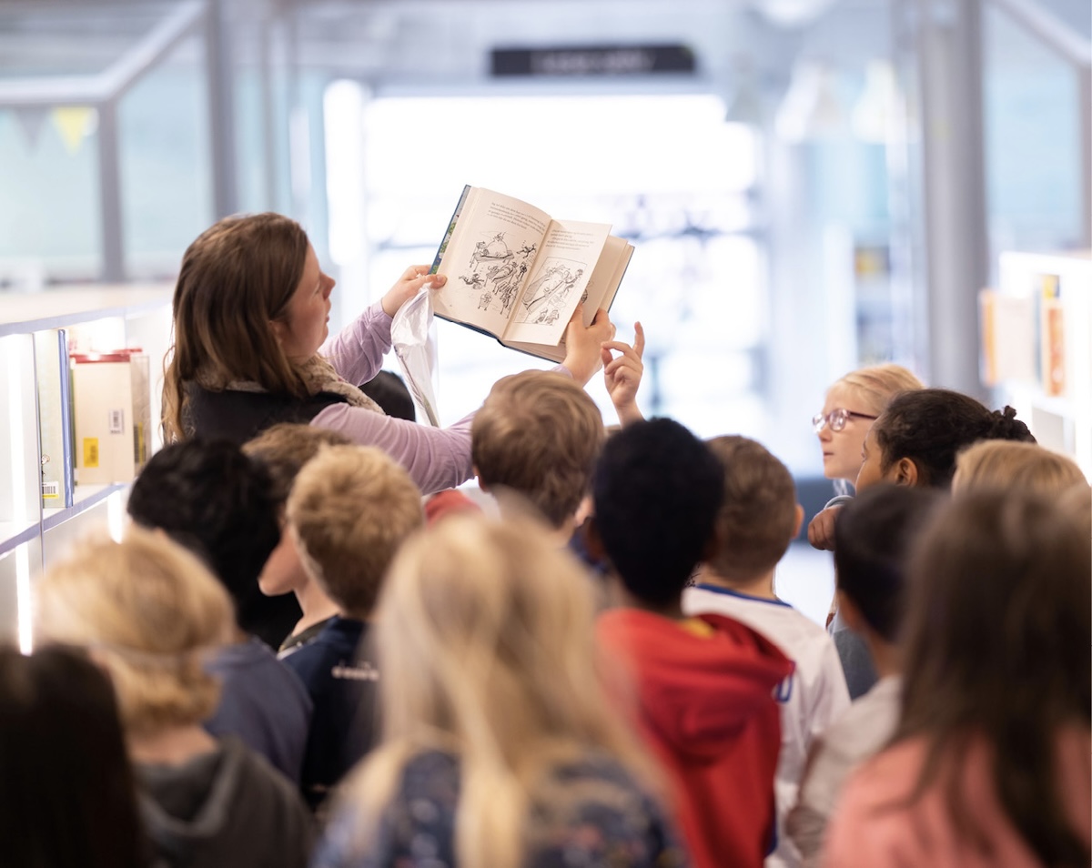 Voksen holder opp en oppslått bok slik at en gruppe barn kan se bildene i boka