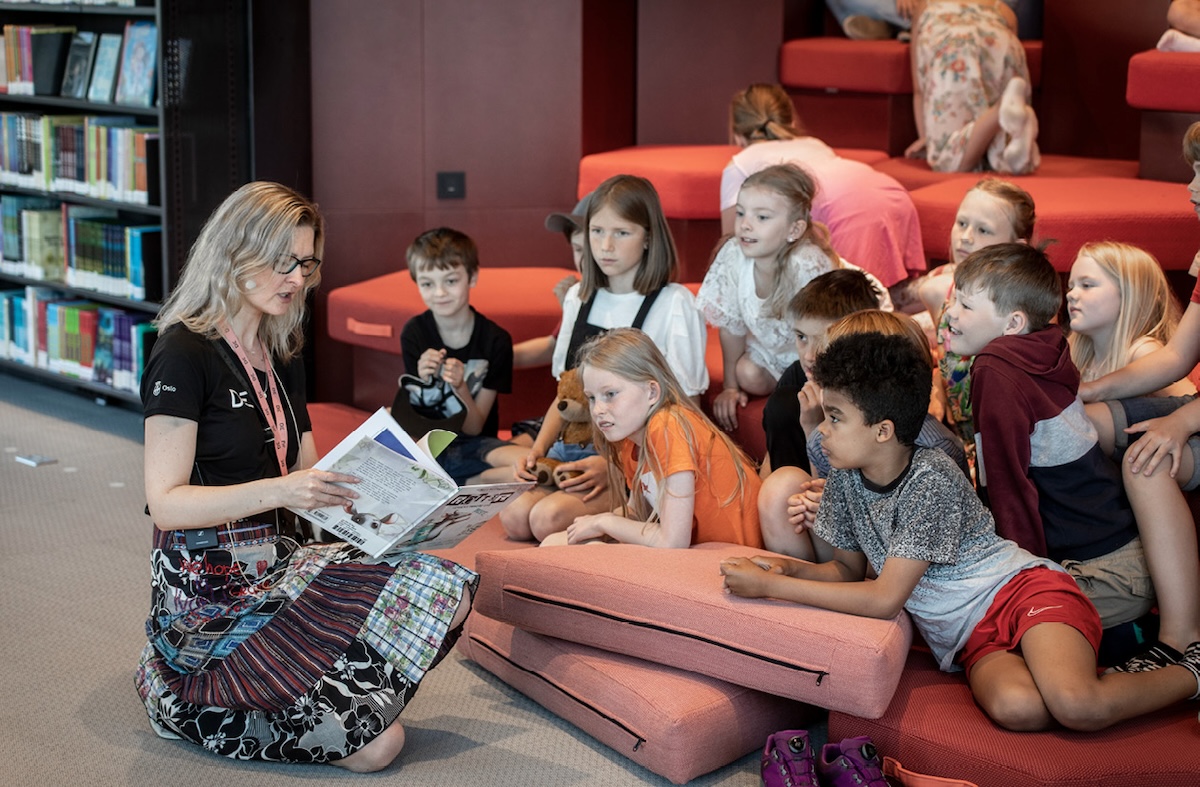En voksen person leser høyt for en gruppe barn i et bibliotek