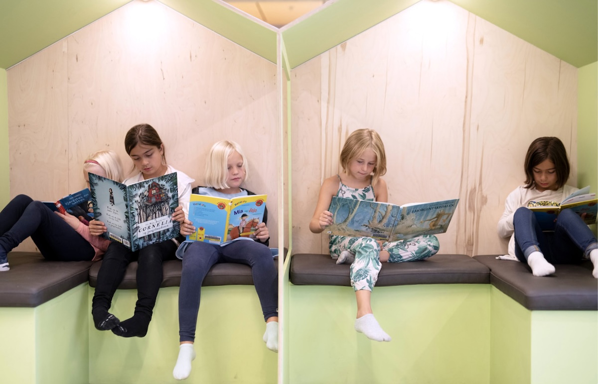 Flere barn sitter i et mindre "leserom" og leser forskjellige bøker i et bibliotek