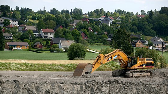 Gravemaskin på åker ved bustadfelt.