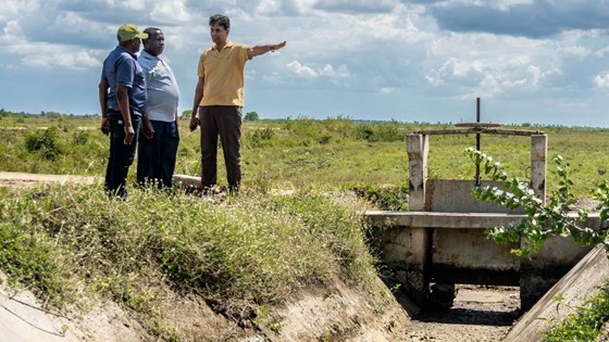 Bilde av James Hangi stående ved el liten elvebredd i solskinn og diskutere med representanter fra Tanzanias landbruksforskingsinstitutt og NIBIO.