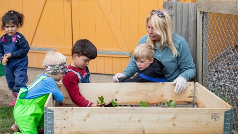 Voksen kvinne sitter med barn rundt en plantekasse.