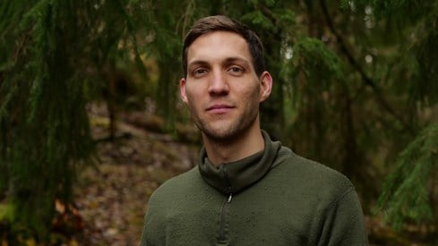 Andreas Bjelland Eriksen i grønn genser. Står i en mørk skog.