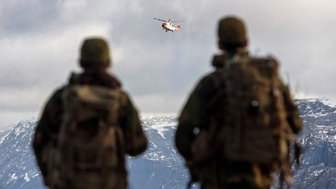 Bildet viser to soldater som ser på et Sar Queen-helikopter i luften