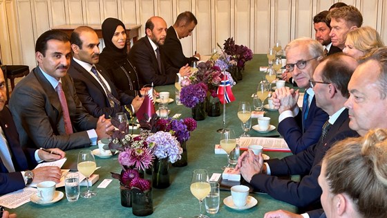 Møtebord med grønn duk. Den norske delegasjonen på høyre side av bordet. Den qatarske på venstre side av bordet. Flagg, blomster og servise.