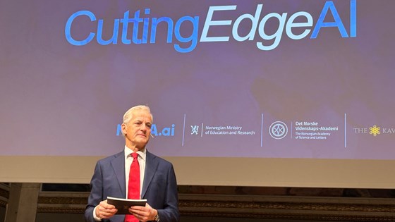 Statsministeren står på scenen. Holder talekort i hendene. Bakgrunn med "CuttingEdgeAI"-logo. 