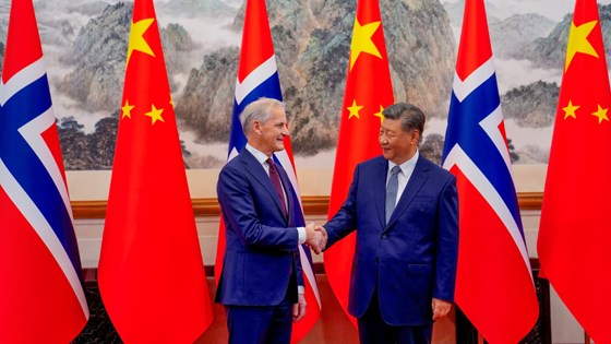 Statsminister Jonas Gahr Støre og Kinas president Xi Jinping står foran norske og kinesiske flagg og tar hverandre i hånda.