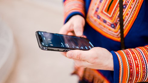 Person med samekofte holder en mobiltelefon