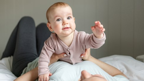 Baby som ligger på magen til en kvinne. Babyen løfter venstre arm og hånd. 