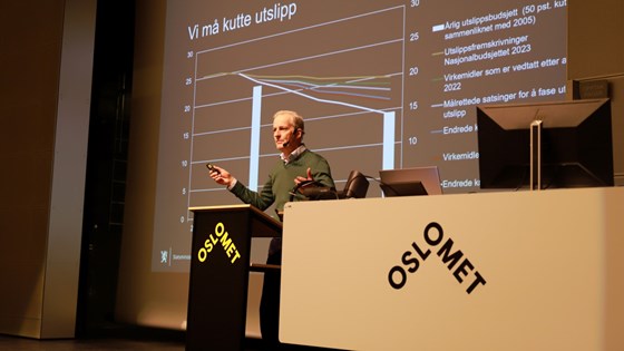 Statsminister Jonas Gahr Støre gestikulerer på en scene med et diagram i bakgrunnen.