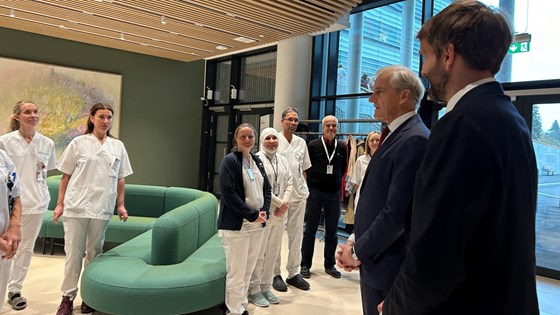 Statsministeren og helse- og omsorgsministeren snakker med ansatte på Radiumhospitalet. I en slags vestibyle. De ansatte i uniformer. Støre og Vestre i dress.