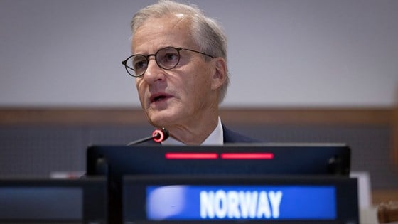 Statsminister Jonas Gahr Støre sitter bak et elektronisk skilt som lyser med Norway i hvit tekst.