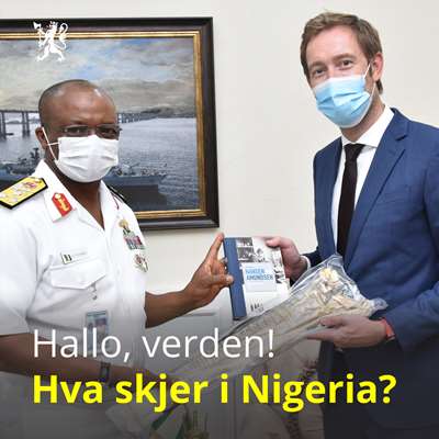 Nigerias marinesjef og Norges ambassadør i Nigeria Knut Eiliv Lein har på munnbind og holder sammen en tørrfisk og en bok.