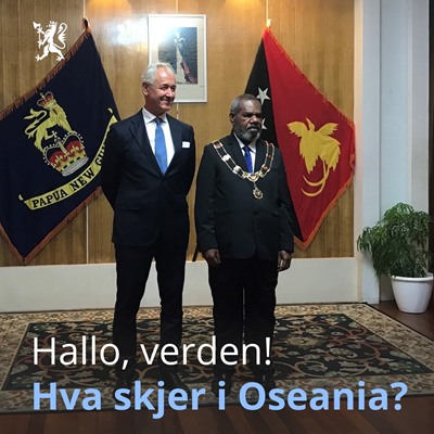 Norsk ambassadør står ved siden av representant fra Papua New Guinea står ved siden av hverandre i dress med landets flagg i bakgrunnen.