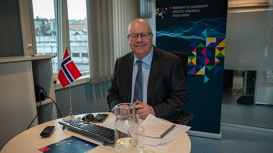 Bilde av Norges Arktis-ambassadør sittende med norsk bordflagg og roll-up med logoen for Norges lederskap